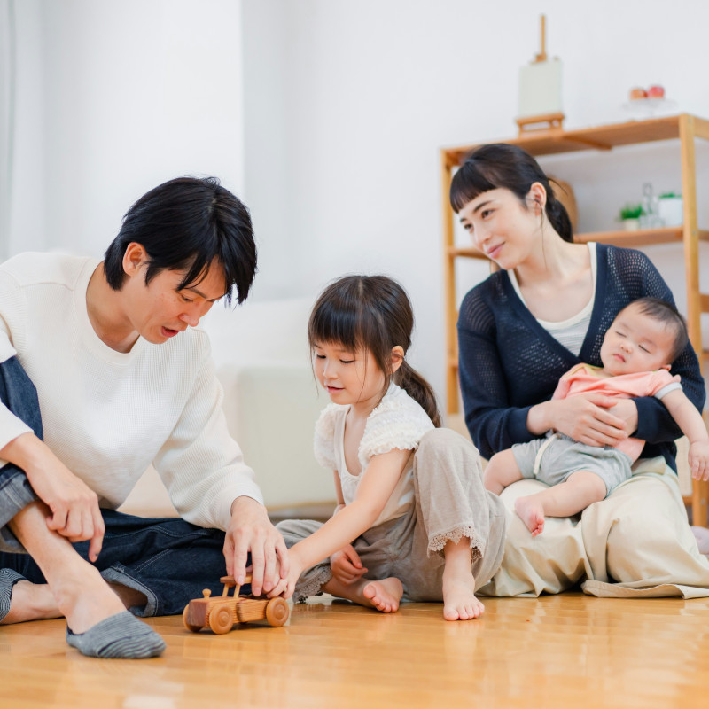 family sitting on wooden floor playing with child